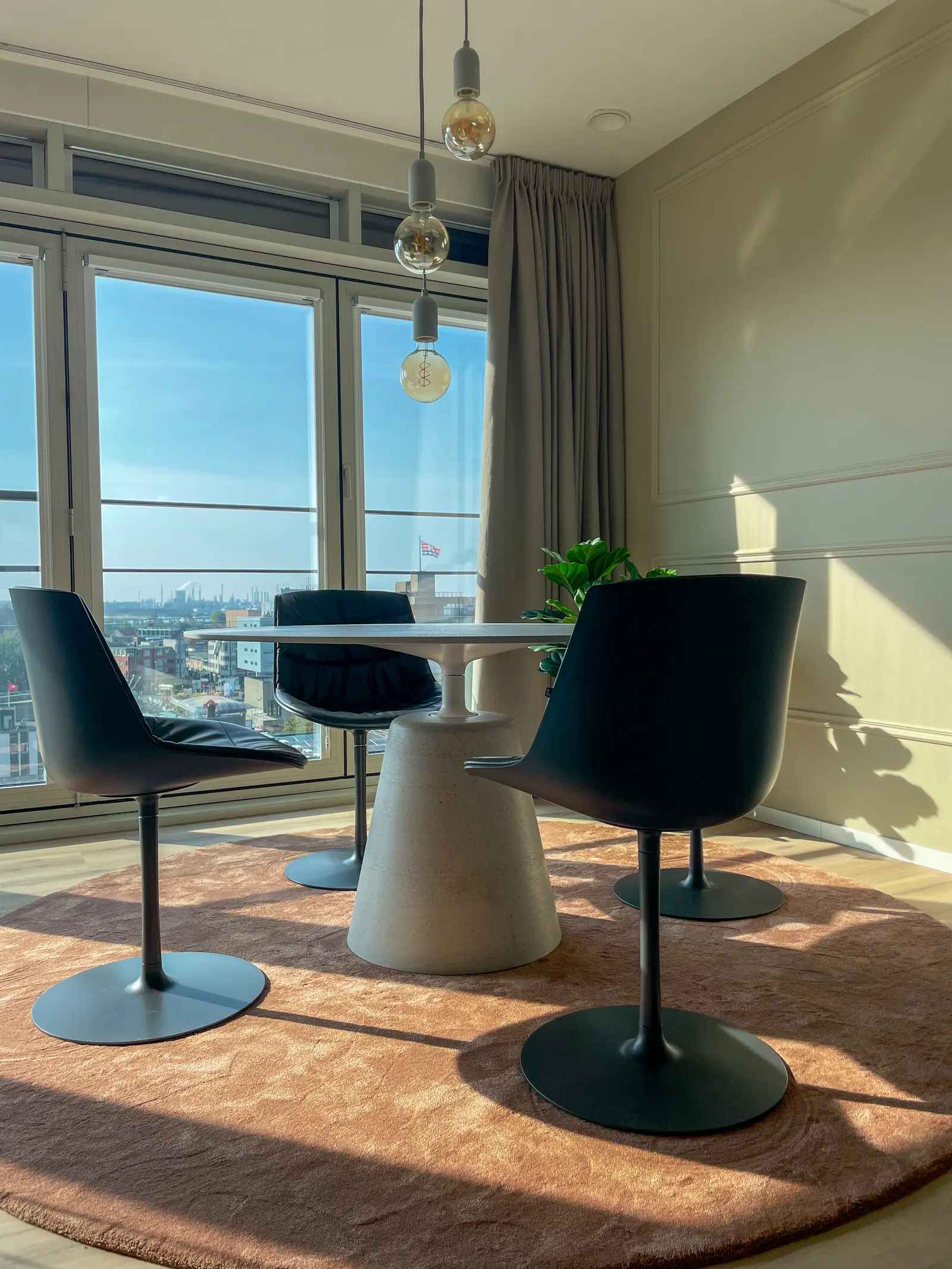 Ronde witte tafel met zwarte kuipstoelen bij het raam, met uitzicht over Terneuzen