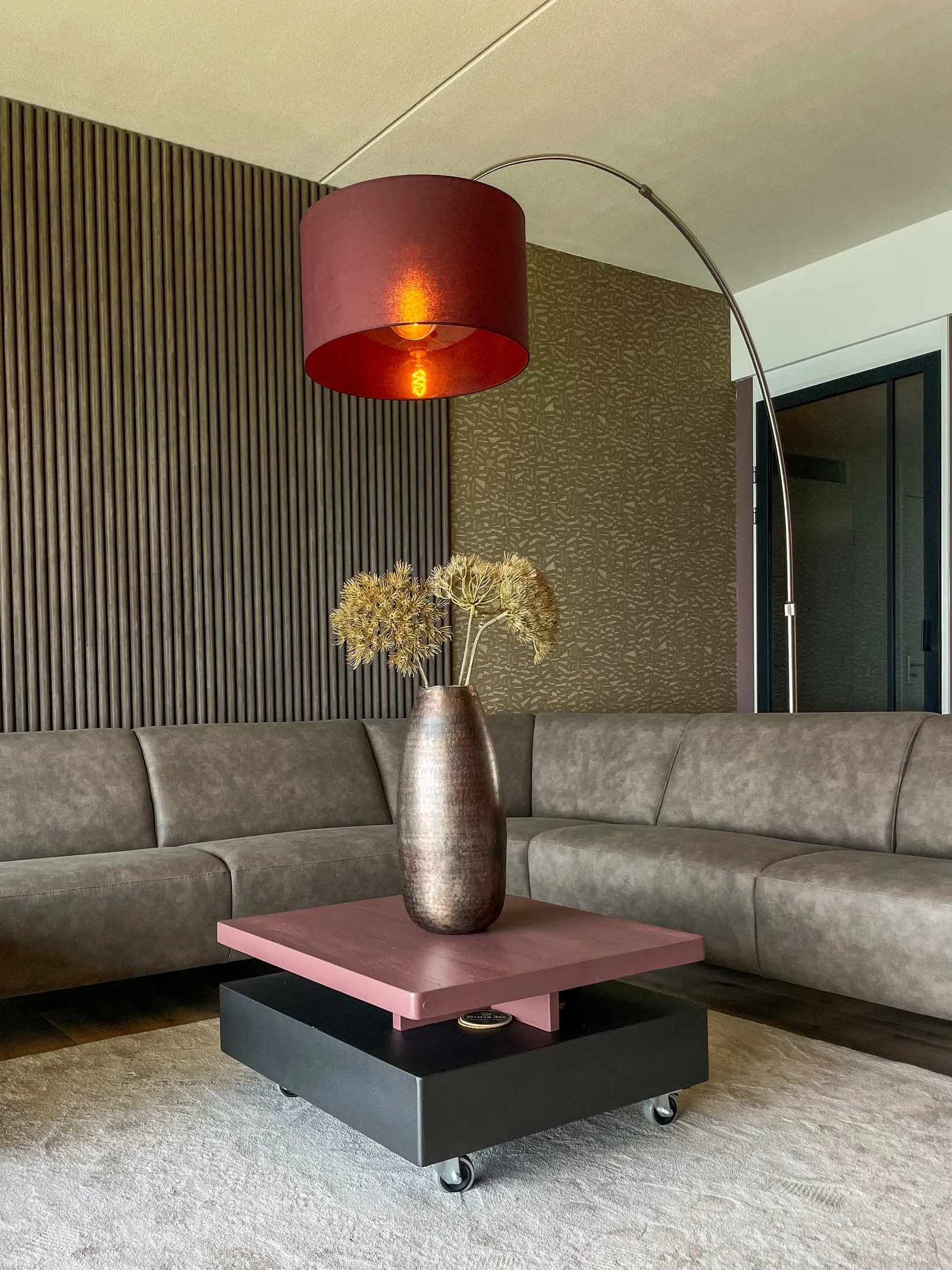 Hoekbank met roze salontafel en booglamp tegen een wand met houten lamellen
