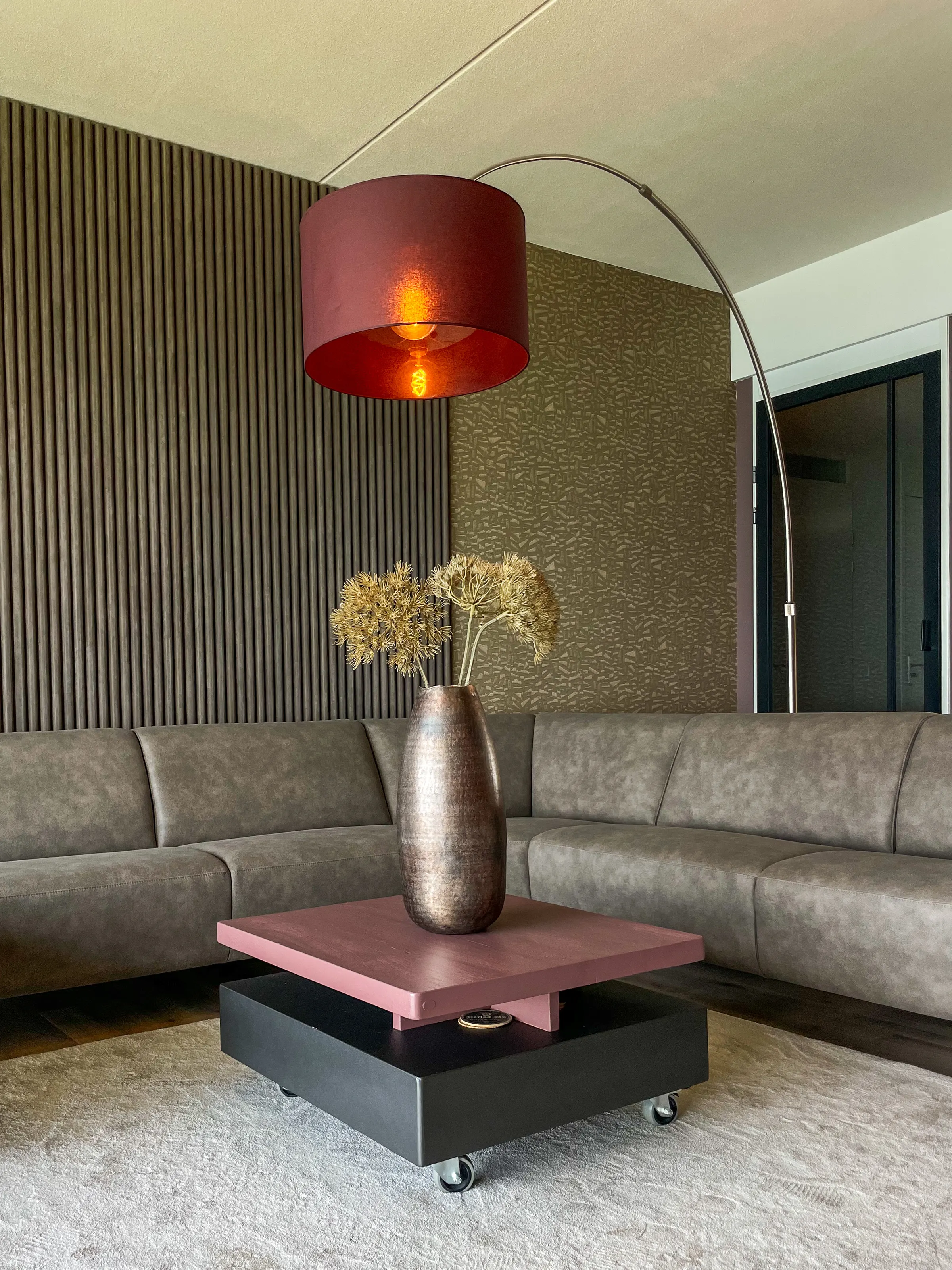Hoekbank met roze salontafel en booglamp tegen een wand met houten lamellen