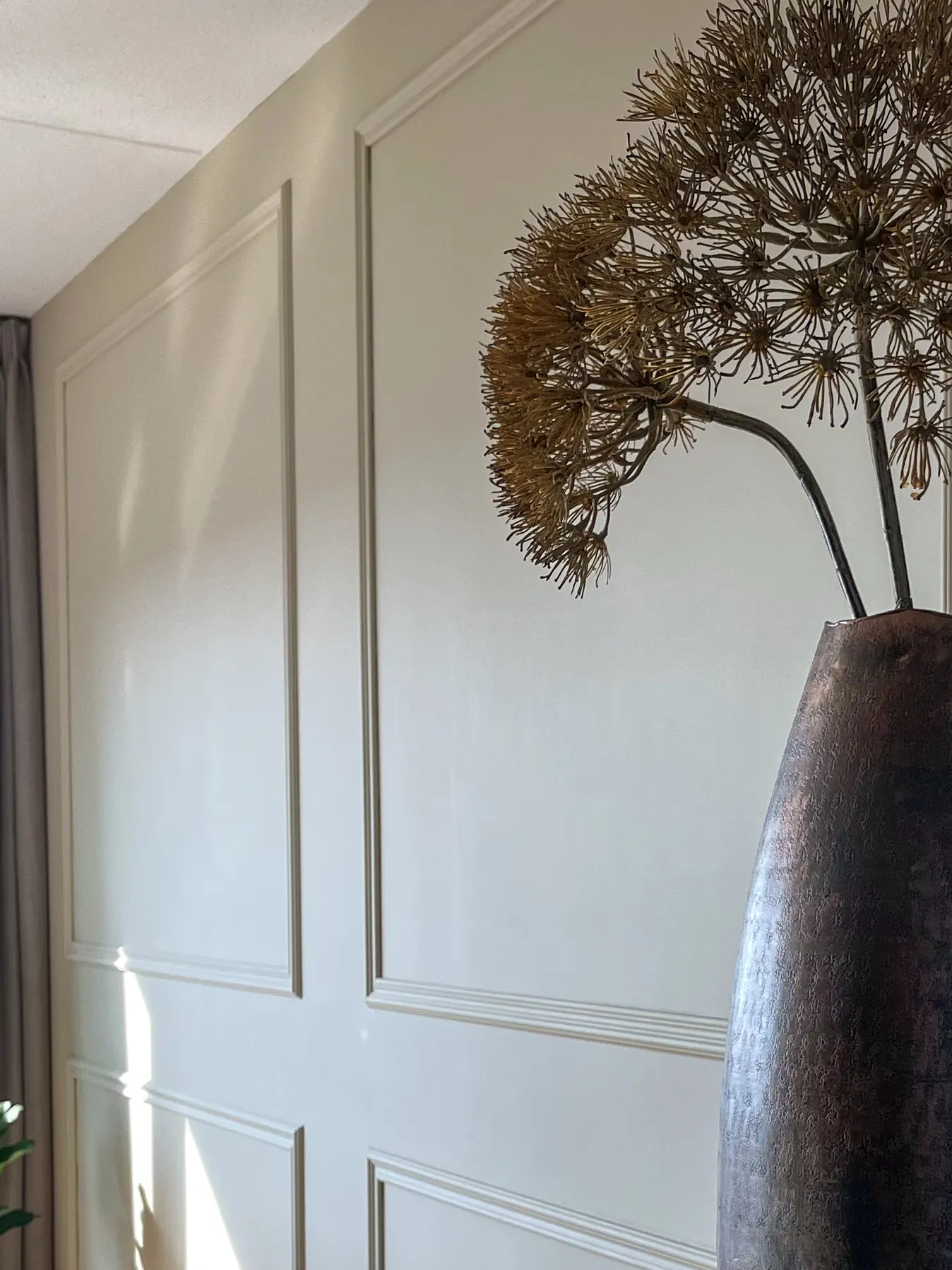 Wandpanelen in een zachte tint met een bronzen vaas en gedroogde bloemen