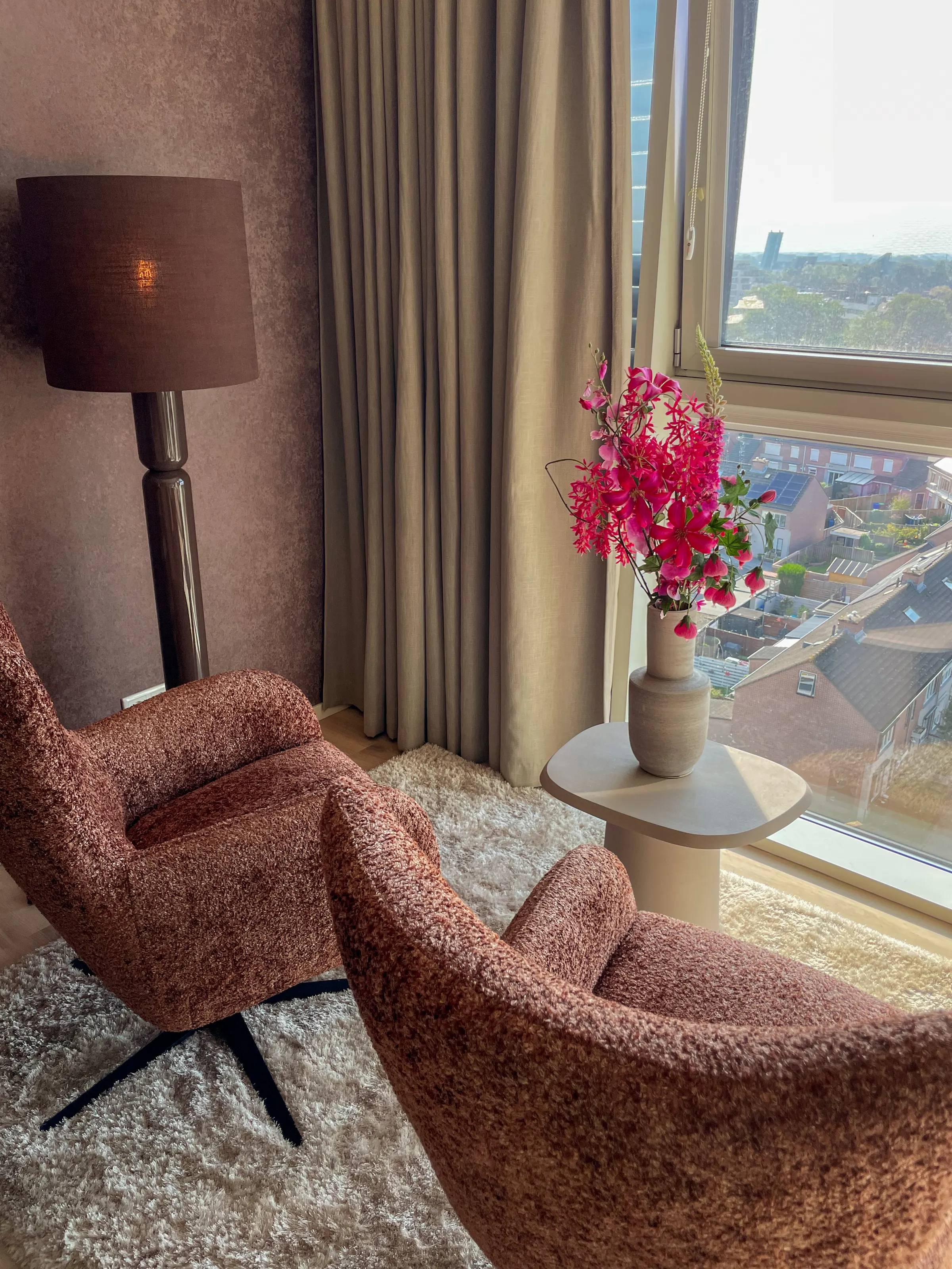 Twee roze-bruine fauteuils bij het raam, voor aubergine behang met een staande lamp